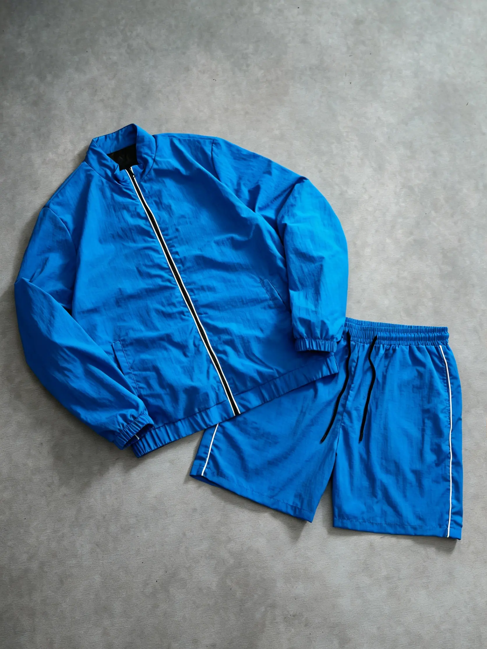 Retro two-piece athletic set with white side stripe and royal blue accents: windproof ruched jacket fabric paired with breathable quick-dry shorts fabric. The entire set features a loose yet fitted silhouette, suitable for urban casual walks, coffee dates