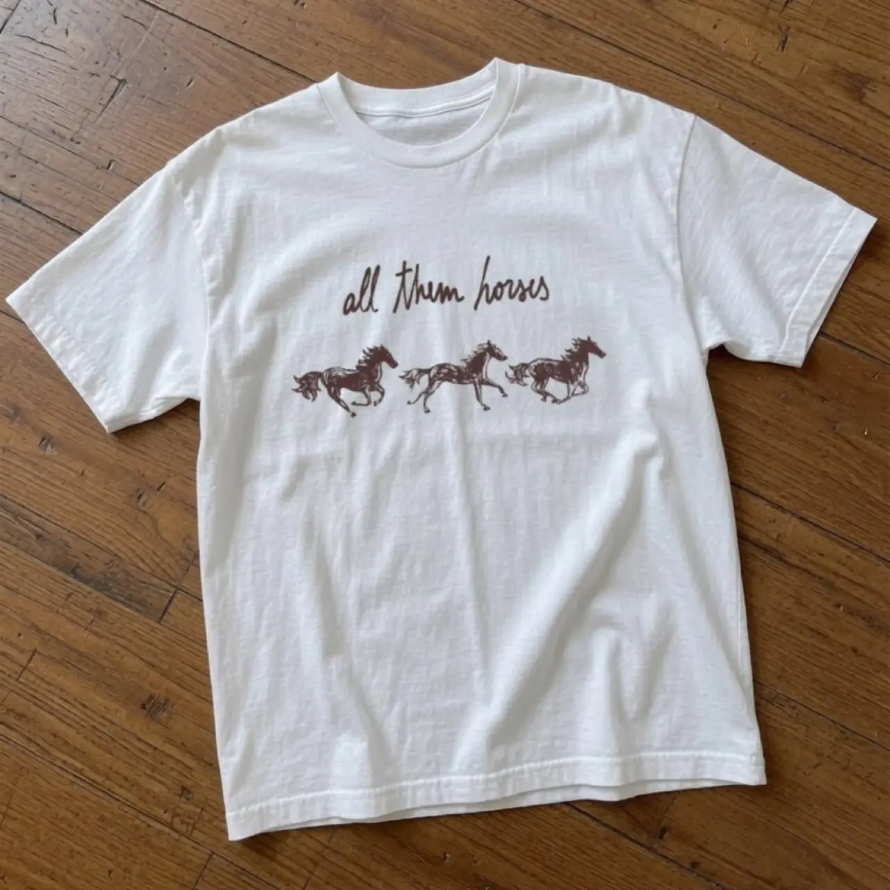White cotton t-shirt with brown graphic of three running horses with the words 'all them horses'