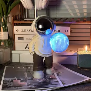 Holding a Dreamy Planet Night Light, an Astronaut-Themed Wireless Bluetooth Speaker, a Desktop Decorative Ambient Lamp, a Creative Gift with USB Charging.