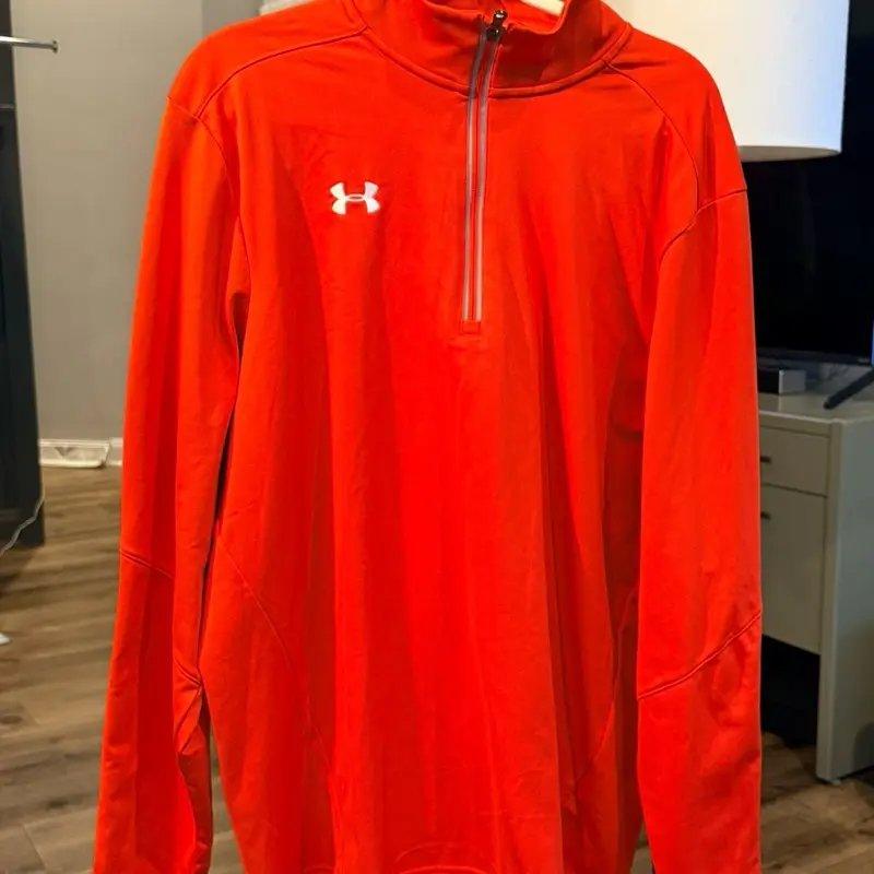Esta es una sudadera naranja con cremallera de un cuarto de la marca Under Armour, estilo Team Tech. Talla xl This is an orange Under Armour quarter-zip sweatshirt, Team Tech style. Size XL.