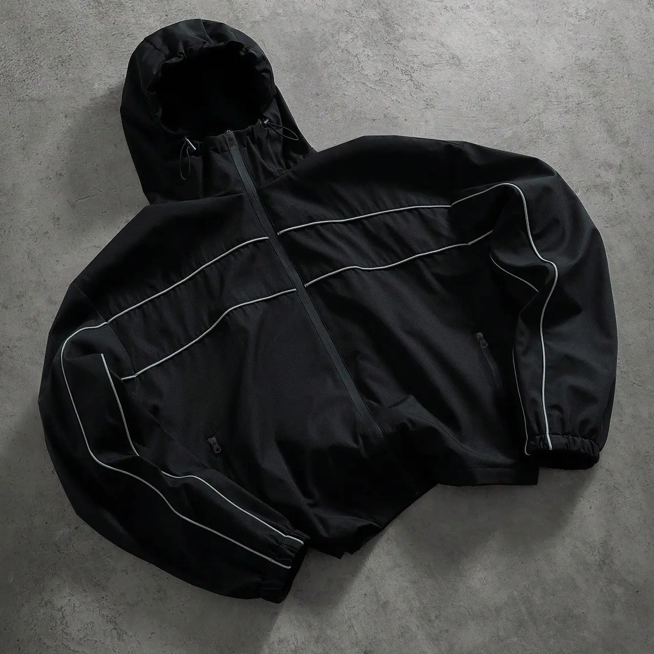 Black windproof hooded jacket with multi reflective stripe details, front zip closure, elastic cuffs, drawstring hood, oversized cropped fit, lightweight woven street athletic outerwear Menswear Coats