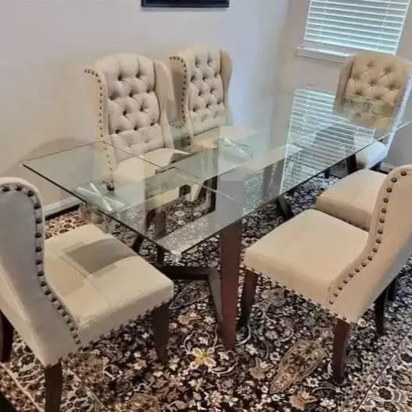 modern dining set features a glass table with a wooden base and beige tufted chairs
