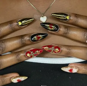 A striking set of pointed nails featuring bold red and black hues with gold accents, showcasing heart and bow designs for a glamorous yet edgy style.