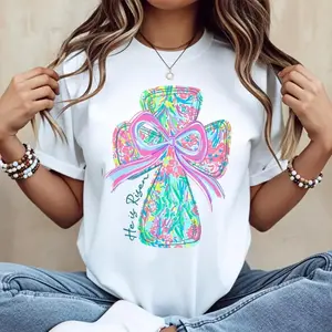Cotton casual round-neck short-sleeve summer T-shirt with vibrant cross and bow design “He Is Risen” printed graphic tee machine washable not dry cleanable made in USA