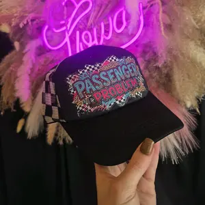 Passenger Problem Black Trucker Hat with Colorful Checkerboard Design and Neon Sign Background