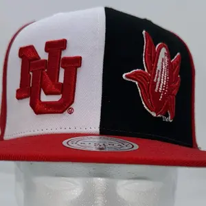 Mitchell & Ness University of Nebraska snapback hat features a unique split-color design with the iconic "NU" logo and a corn mascot graphic.