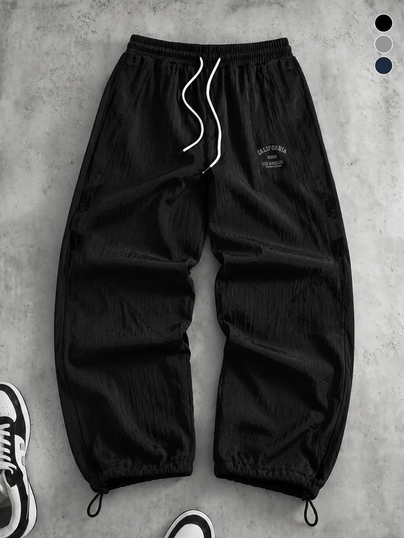 Men’s black textured drawstring jogger sweatpants with small embroidered logo, loose casual athletic long pants, American vintage minimalist style.