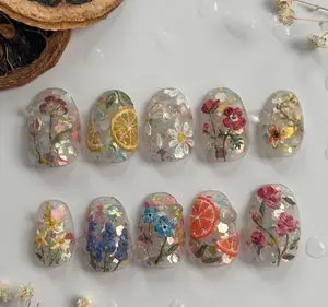 Fresh botanical nails with pressed flowers, citrus slices, and iridescent flakes encapsulated in clear gel for a bright, garden-inspired spring aesthetic