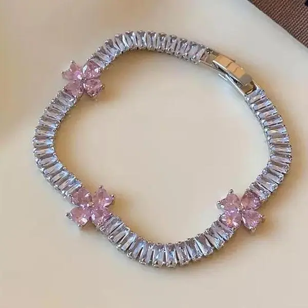 Elegant tennis chain bracelet fully paved with rectangular baguette clear sparkling crystals, adorned with three delicate pink crystal flower accents. Silver polished finish with firm snap clasp, flexible wearable chain, sweet refined feminine style.